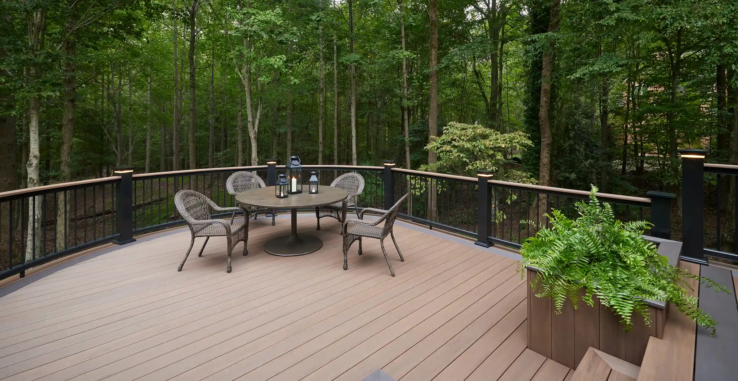Photo of an elevated deck in a wooded area with curved deck railing, built-in planter box, deck steps, and outdoor furniture