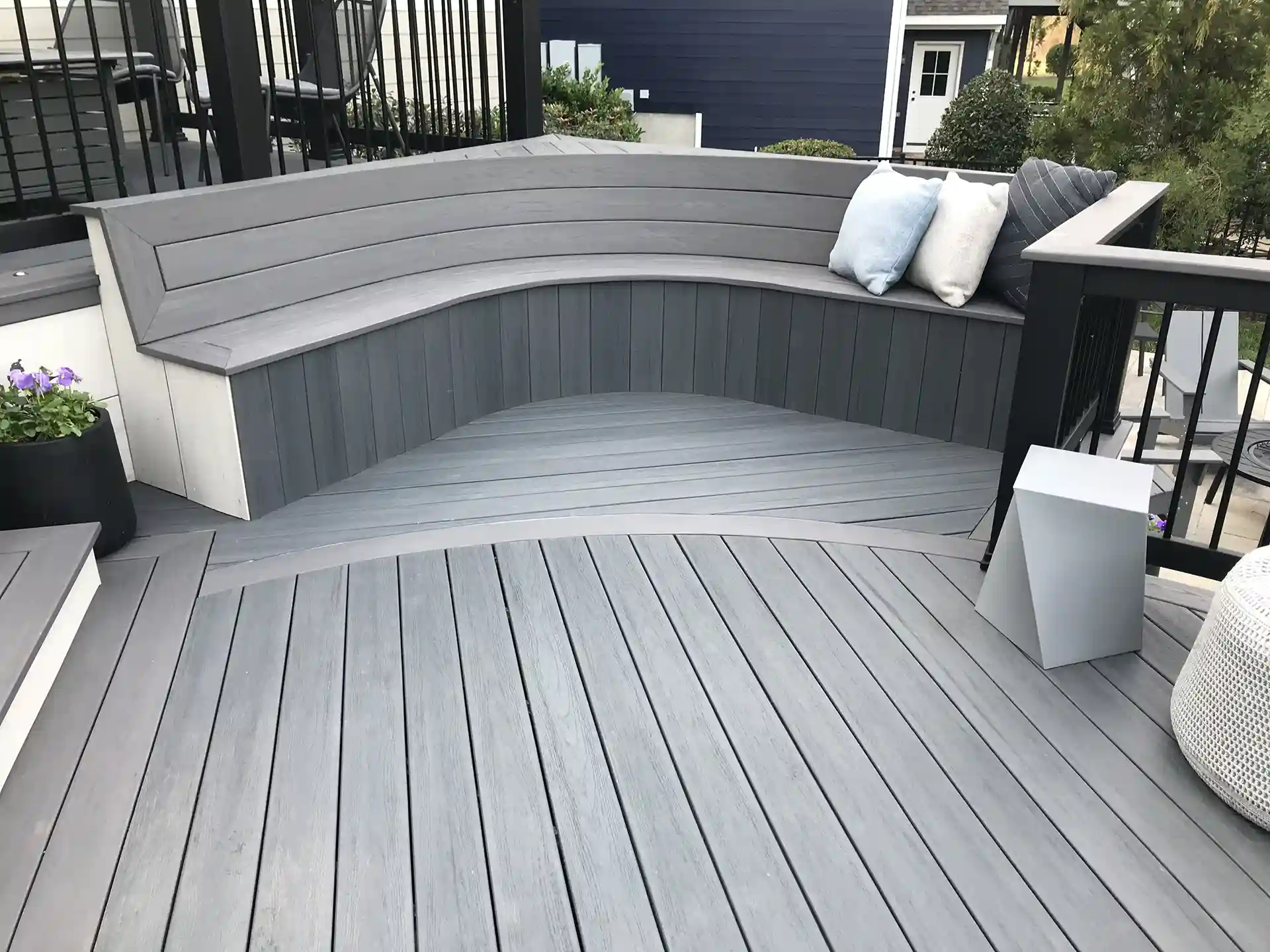 stylish gray composite deck with curved built-in seating, accent pillows, and planters.